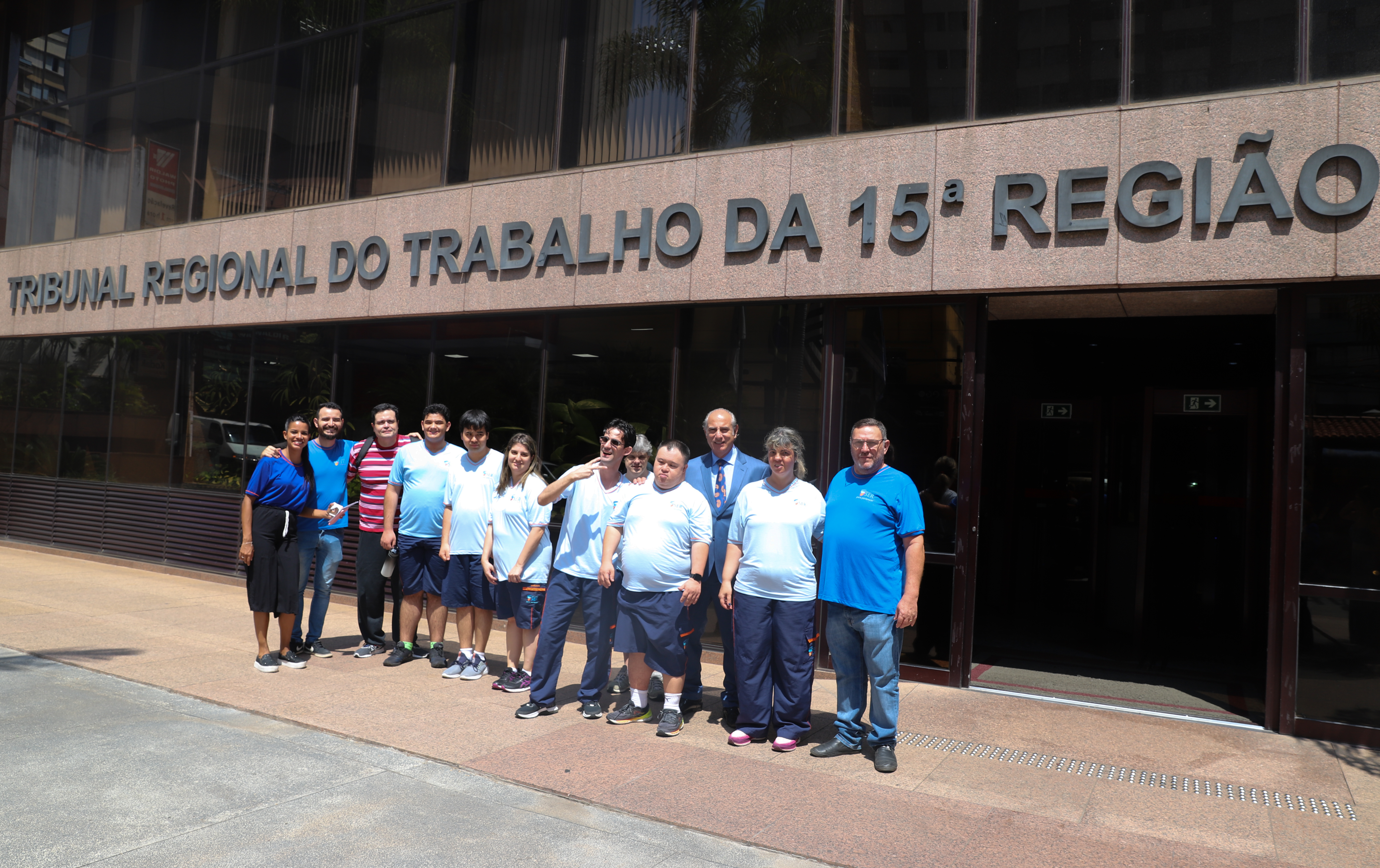 Doze pessoas em frente a fachada do tribunal, sendo sete alunos uniformizados, acompanhados de professores e do desembargador Fabio Aguiar