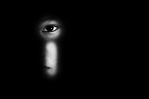 foto em preto e branco exibe uma criança olhando pela fechadura