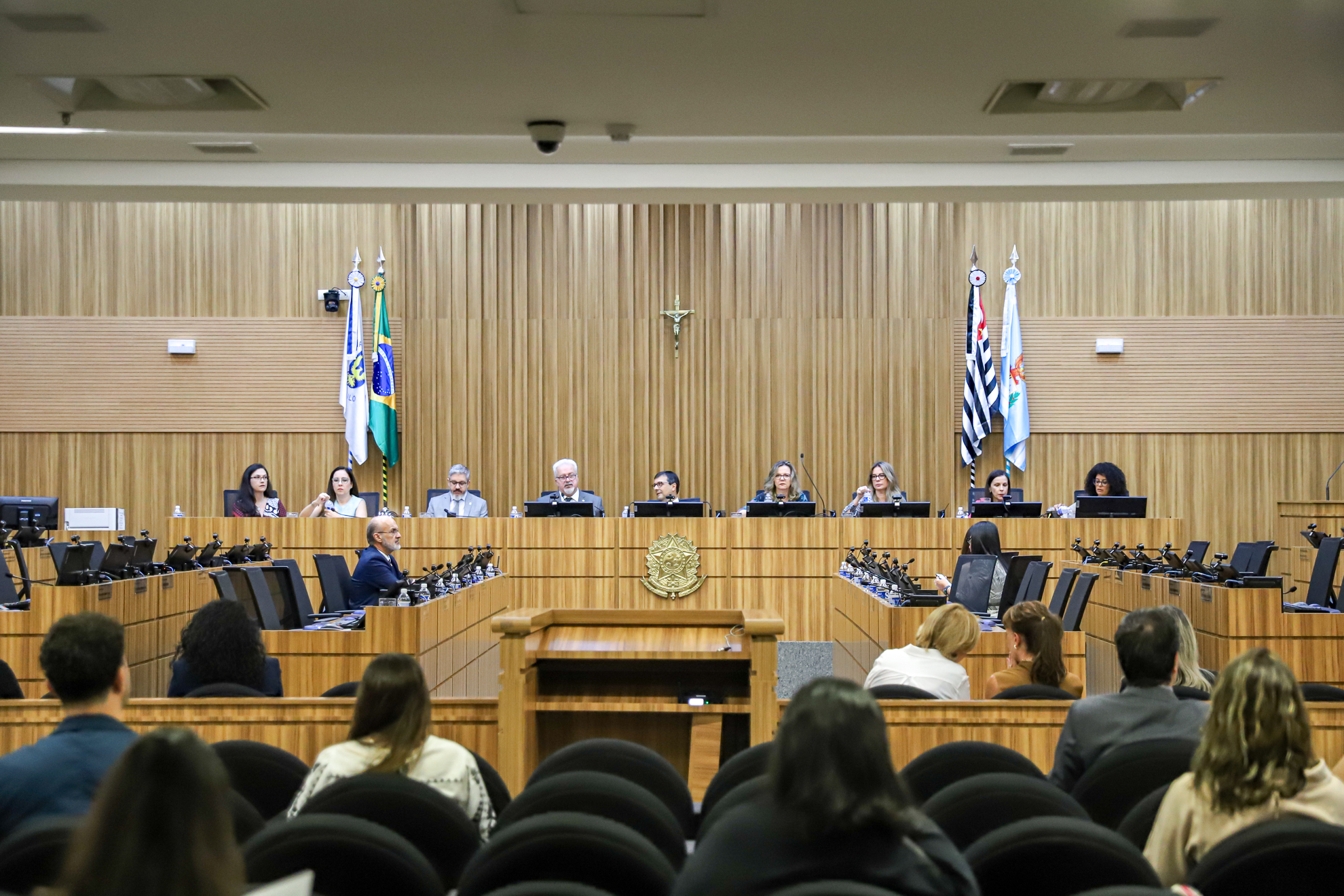 Foto da mesa alta, no Plenário. Nove pessoas, sendo seis mulheres sentados à mesa alta, sendo observados pelo público.