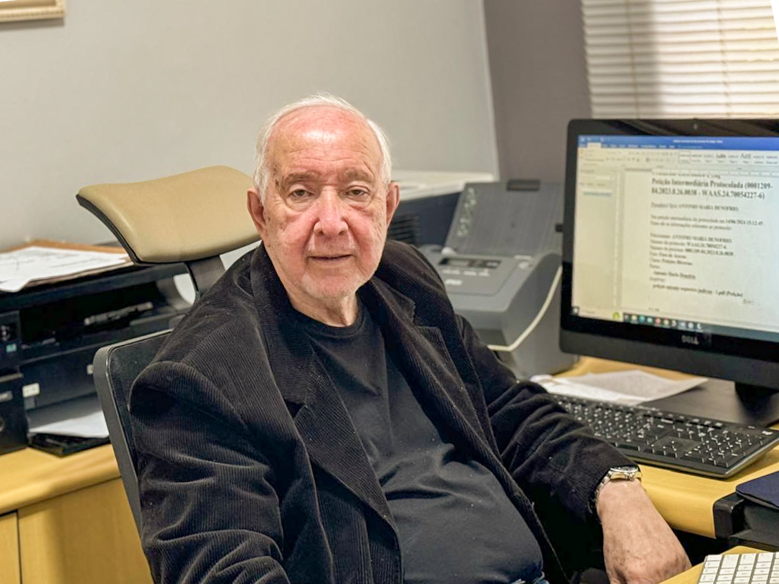 Foto posada do advogado Denófrio, sentado, em seu escritório, ao fundo a tela do computador.