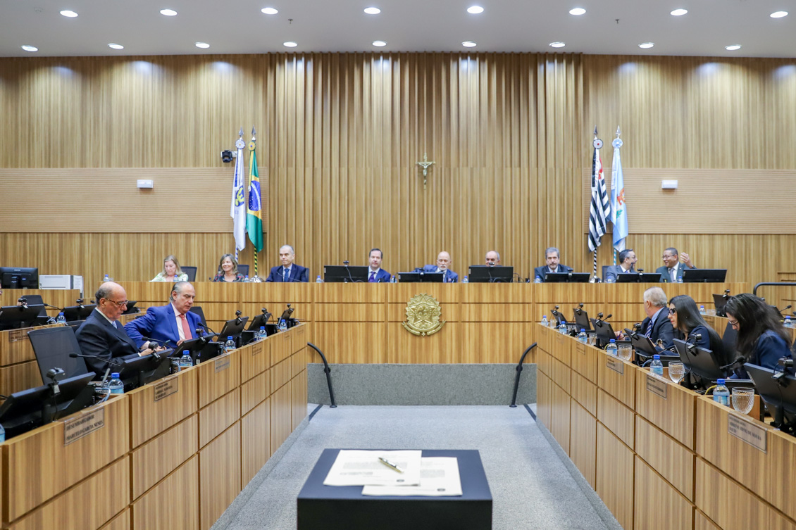 Vista frontal do Plenário do TRT-15, com juízes em uma tribuna na frente e em duas nas laterais. Ao centro, vê-se uma mesa com duas folhas de papel e uma caneta.