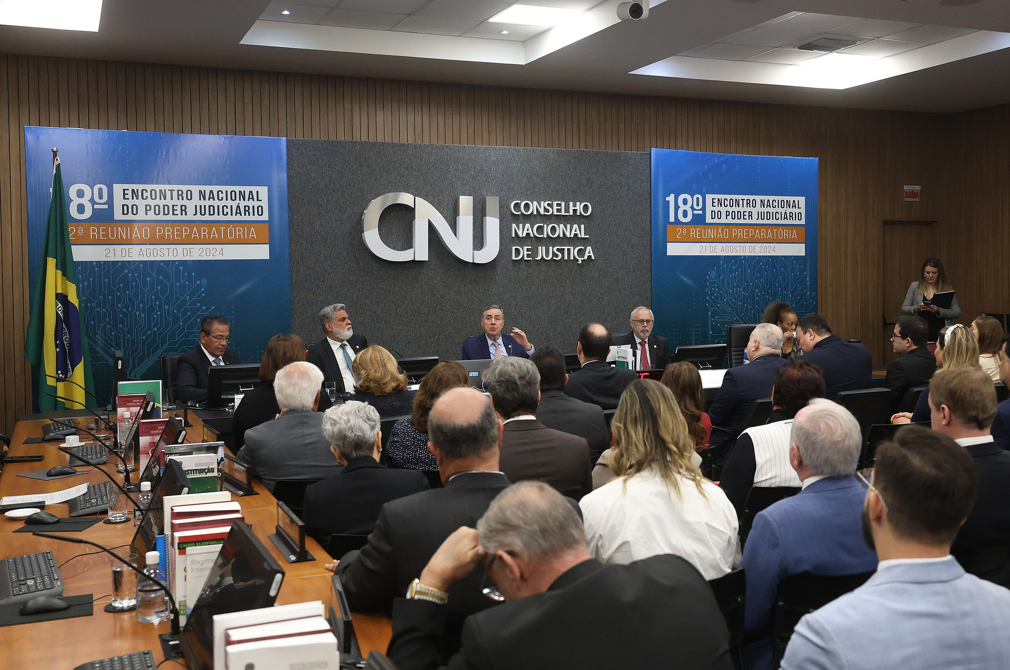 Ministro Barroso preside reunião do centro da mesa alta, ao lado do presidente do TST. A plateia acompanha em auditório do CNJ