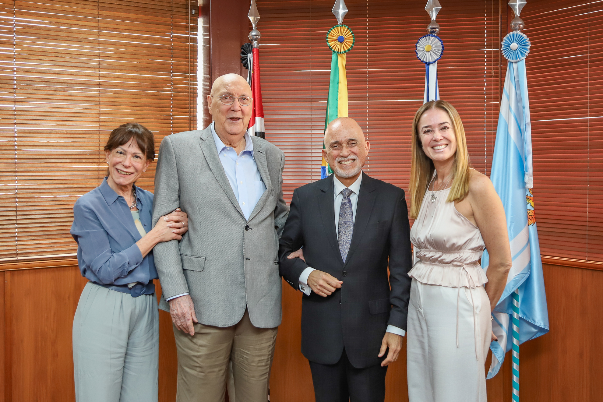 o reitor João Manoel e a Dra. Maria Inês estão com o desembargador Samuel e a juíza Daniela no gabinete da Presidência, em frente as bandeiras.