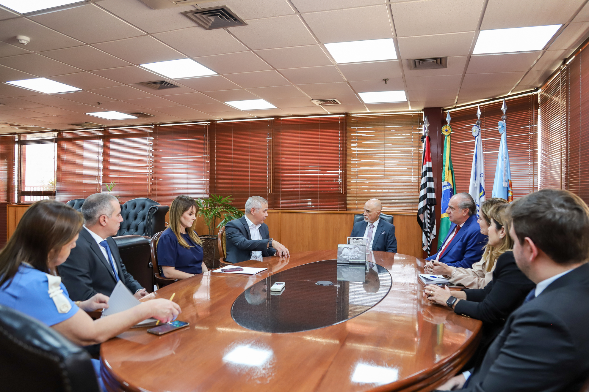 ParaTodosVerem: nove pessoas estão reunidas ao redor de uma mesa de madeira. 