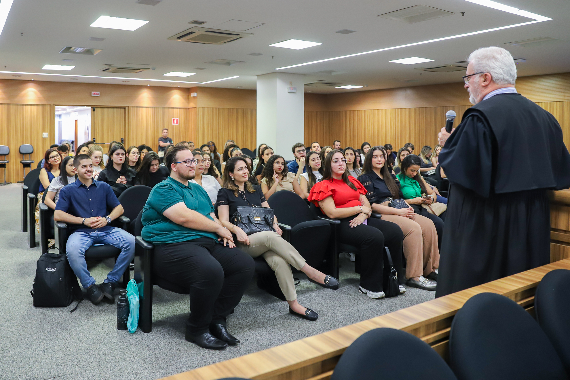 Estudantes estão sentados nas cadeiras do plenário, ouvindo as orientações do desembargador Luiz Paim Lobo