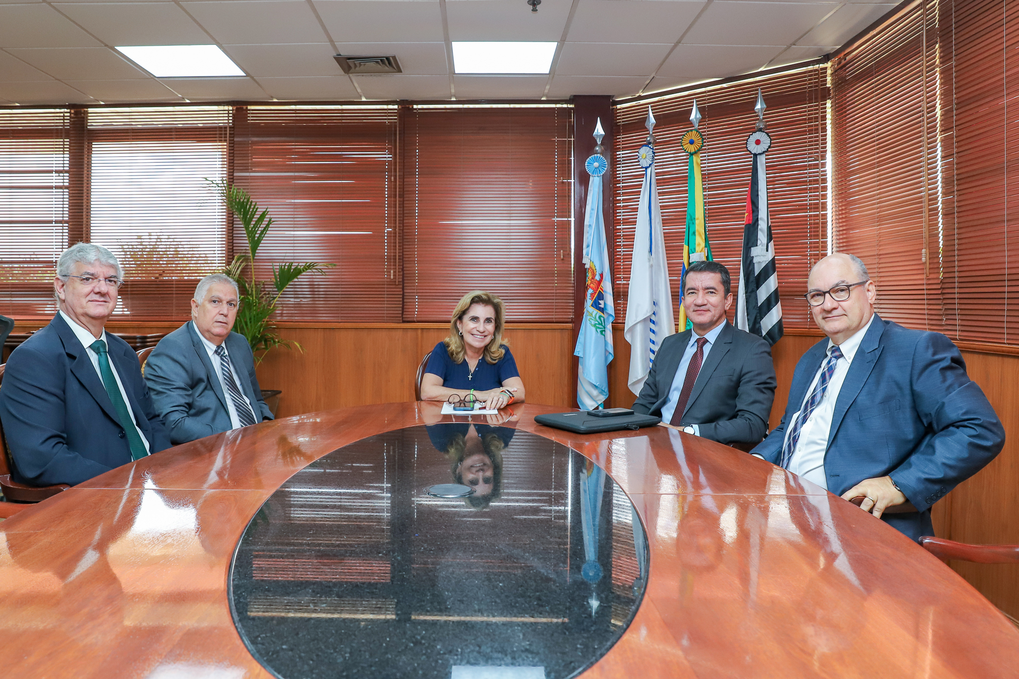 Dirigentes estão sentados em torno de uma mesa de madeira oval