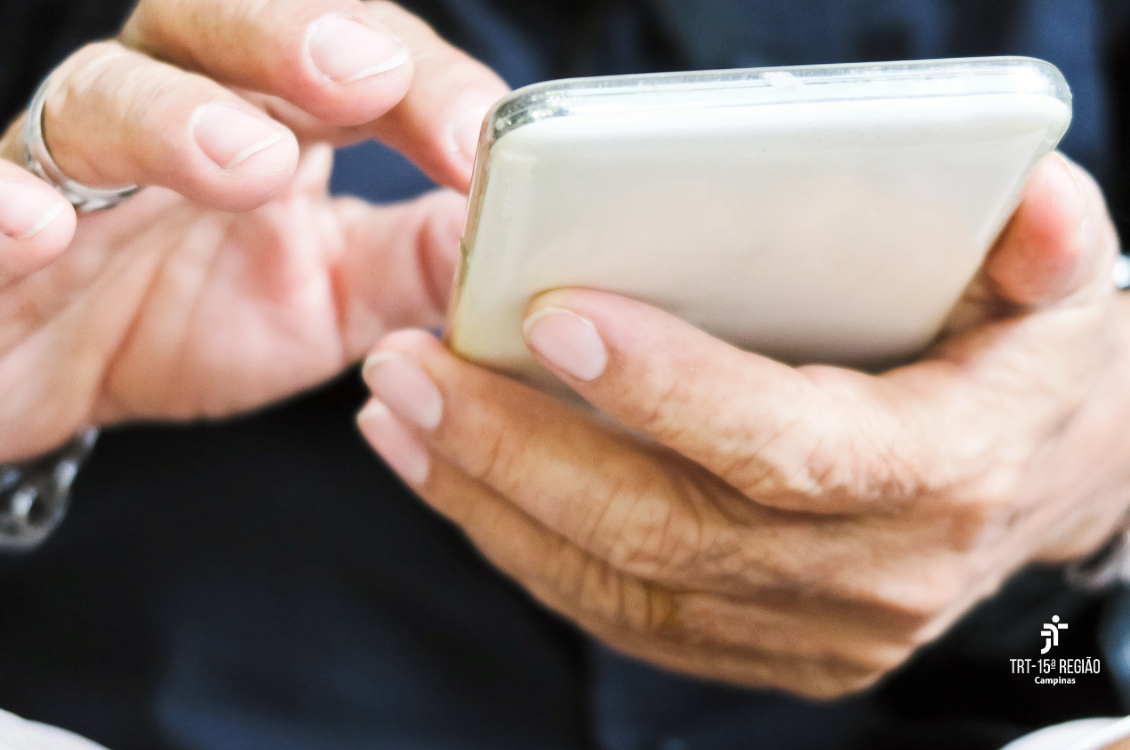 duas mãos masculinas manipulam um celular. No rodapé direito, a logomarca do TRT-15.