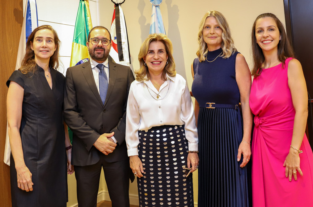 Dra. Ana Paula com os quatro juízes posam para foto de pé em frente as bandeiras