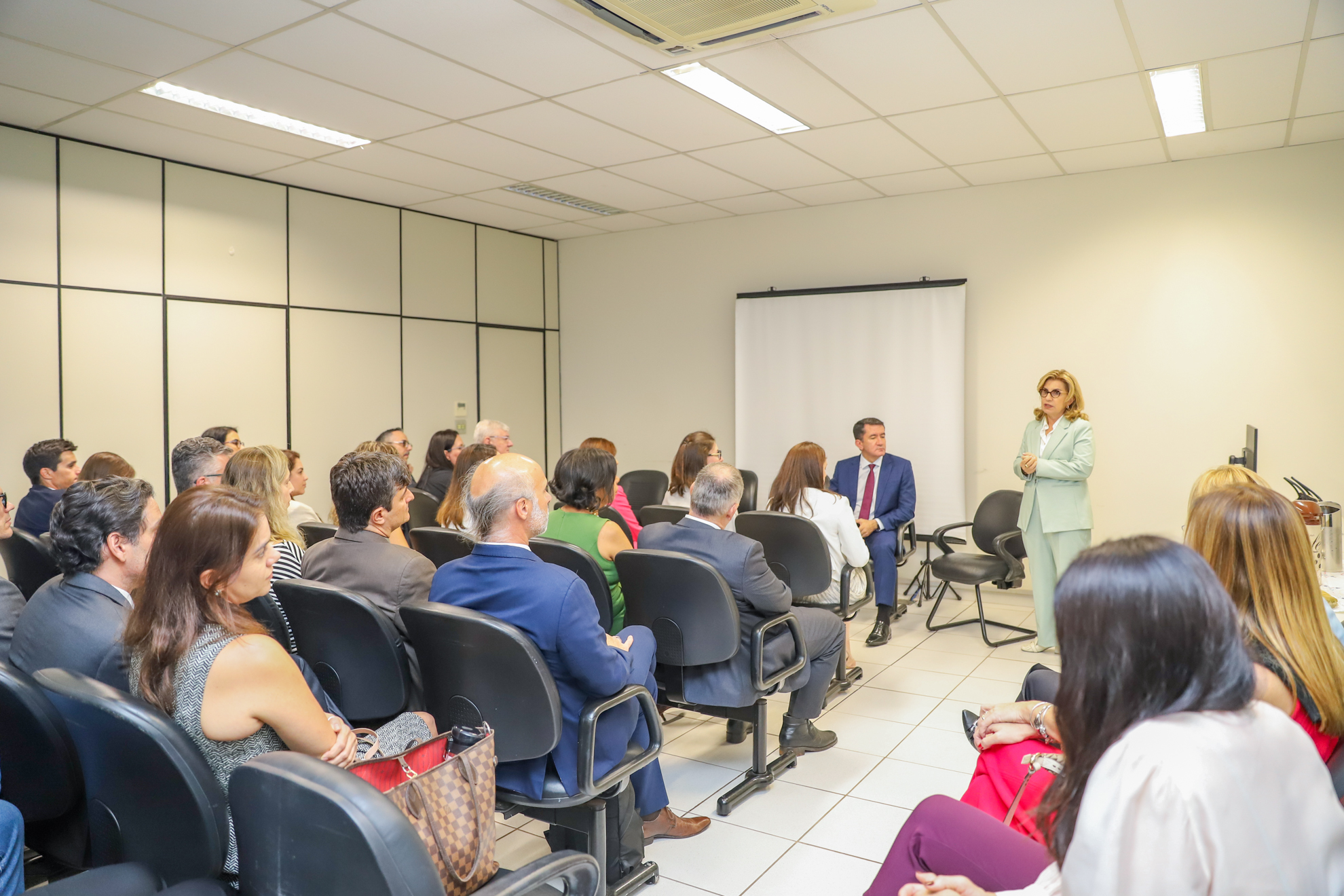 Dra. Ana Paula está no canto direito da tela, gesticulando, sendo observada pelos juízes sentados no auditório. 