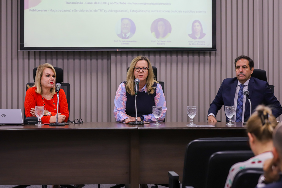A foto retrata três pessoas, duas mulheres e um homem, todos sentados.