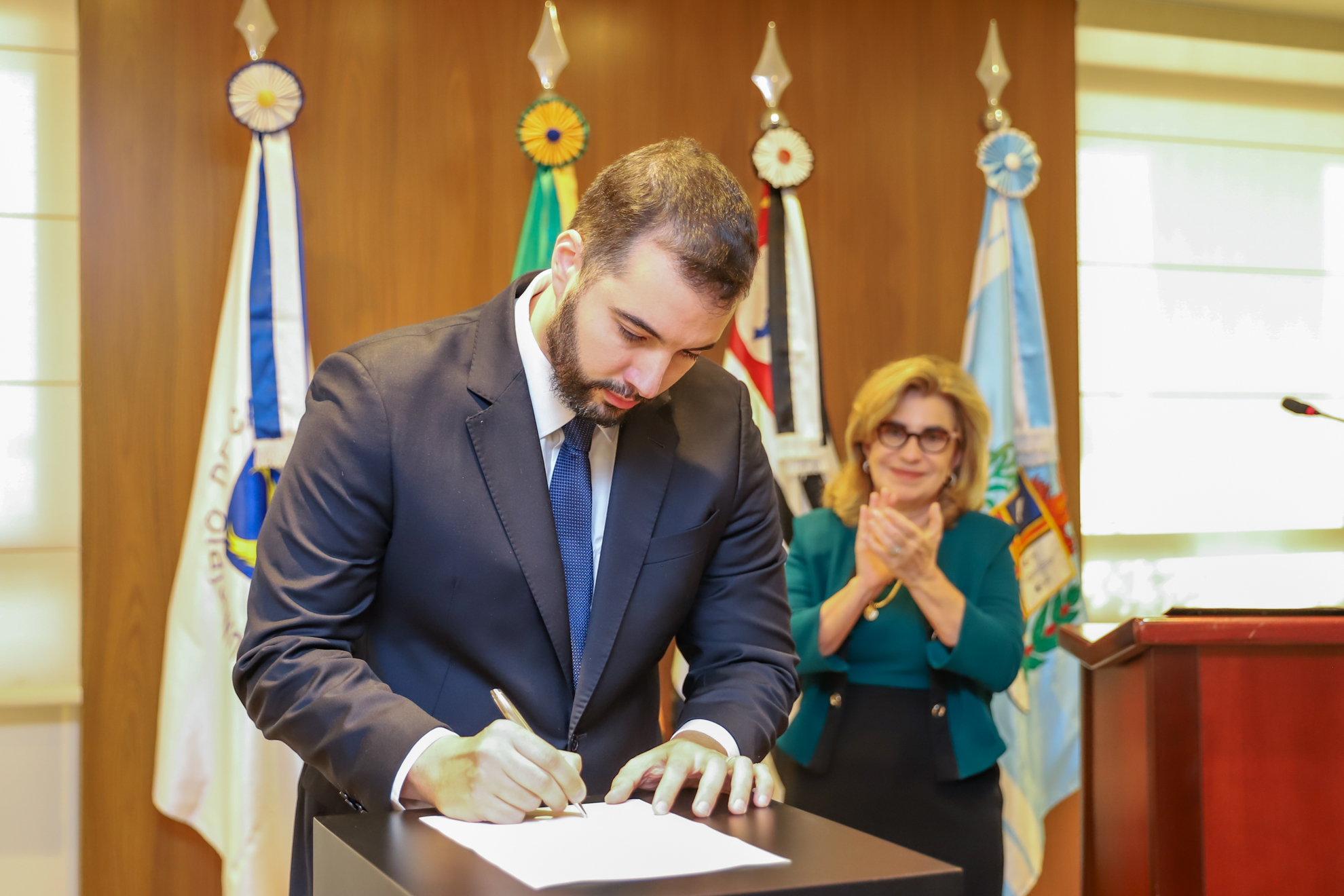 O magistrado Felipe assina o termo de posse sendo observado pela desembargadora Ana Paula.