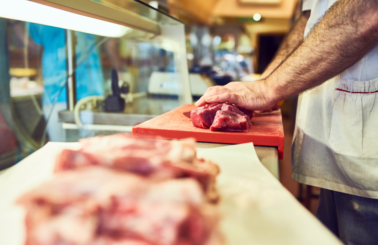 A foto retrata um açougueiro cortando um pedaço de carne.