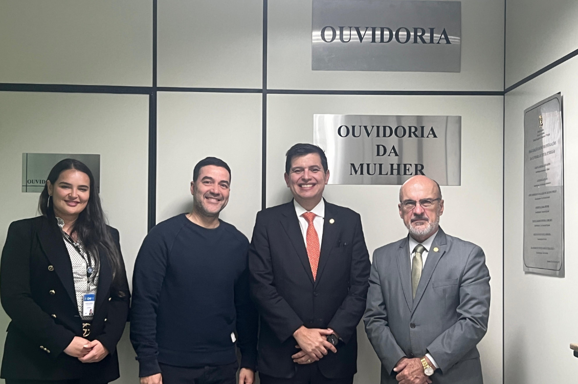 foto posada do ouvidor, de sua assessora, do Dr. Edmundo e de Alan, com as placas Ouvidoria e Ouvidoria da Mulher ao fundo
