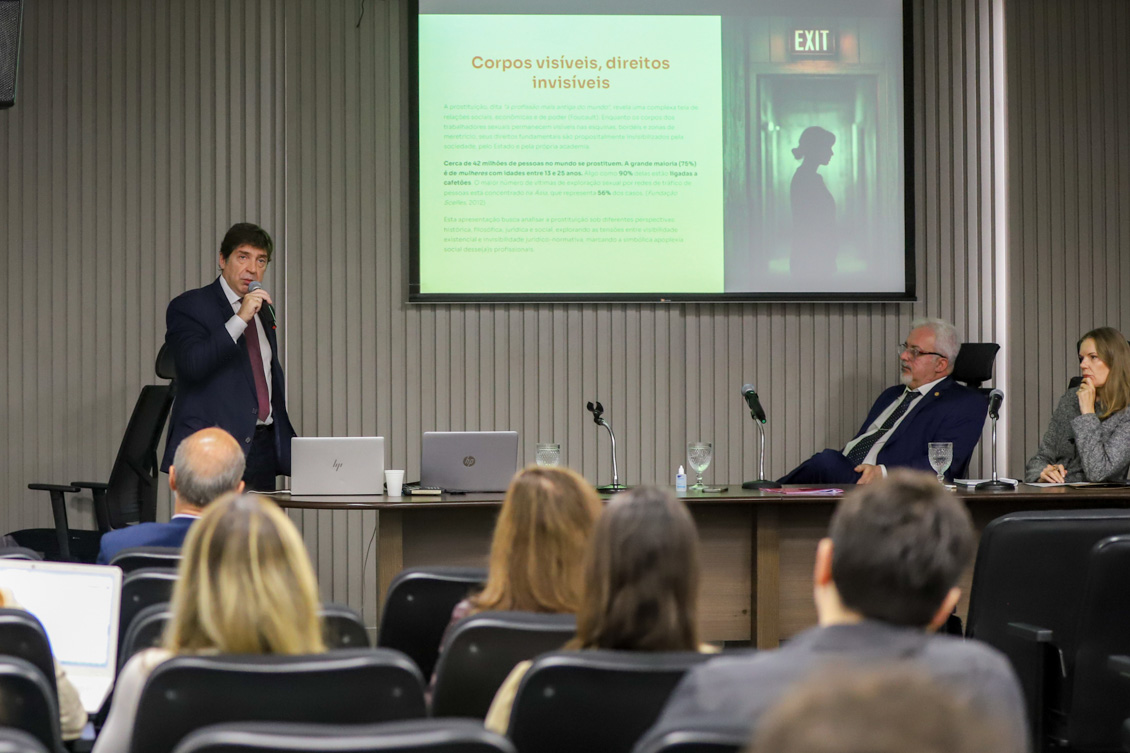 imagem geral do auditório com os palestrantes ao fundo e o público presente em primeiro plano. No telão, o tema da palestra