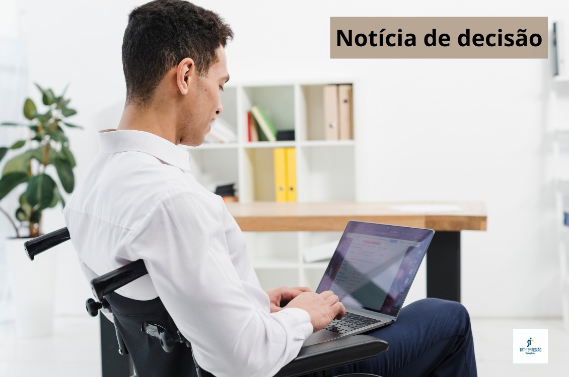 A foto retrata um rapaz sentado na cadeira de roda, digitando em um notbook.