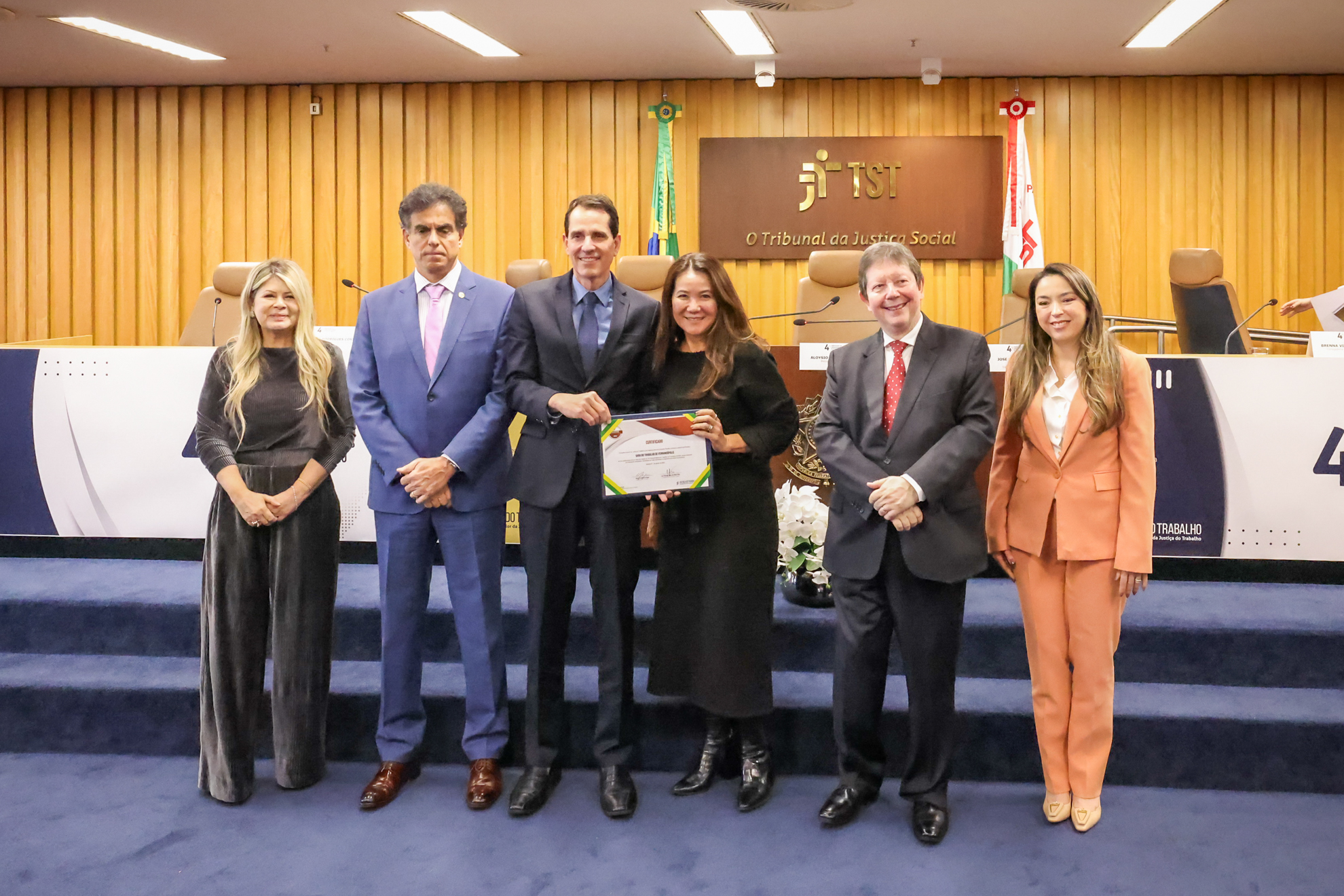seis pessoas posam em pé para foto. Duas estão segurando um certificado.