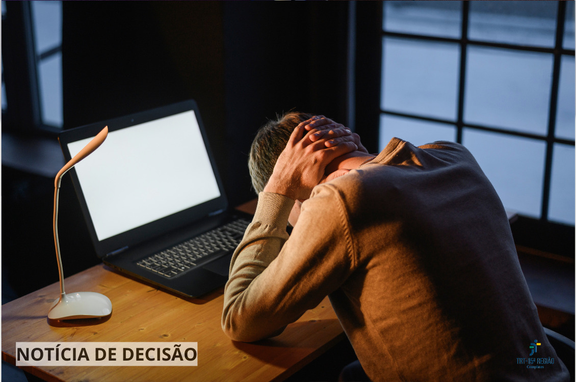 homem está cabisbaixo, com as mãos cruzadas no pescoço, em frente a um notebook