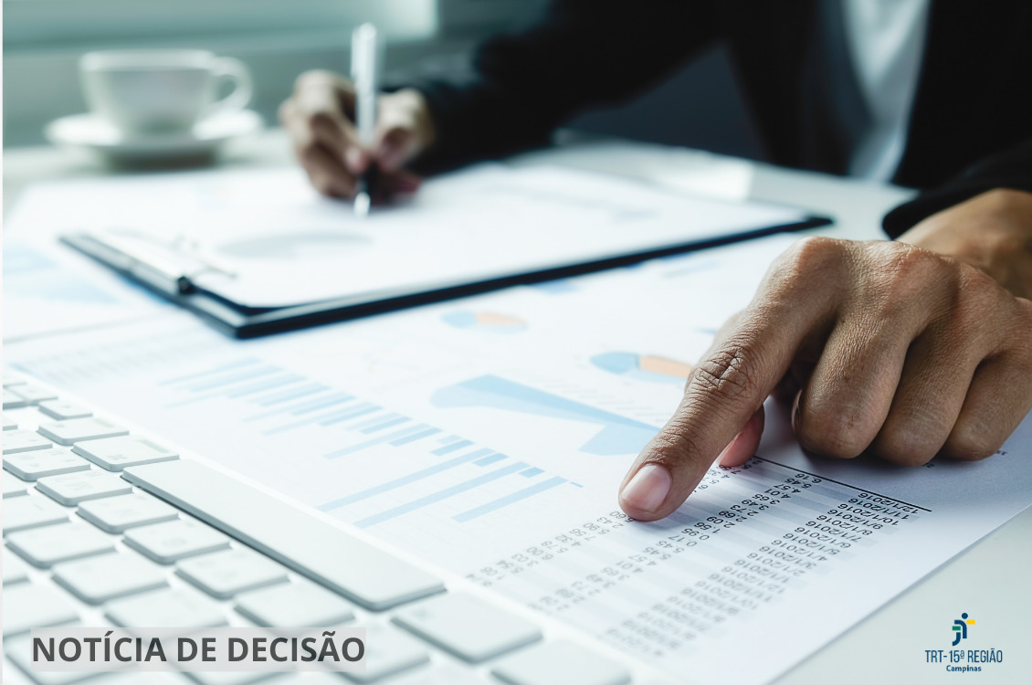 mãos masculinas analisam documentos e escrevem numa planilha sobre a mesa, que também tem um teclado branco