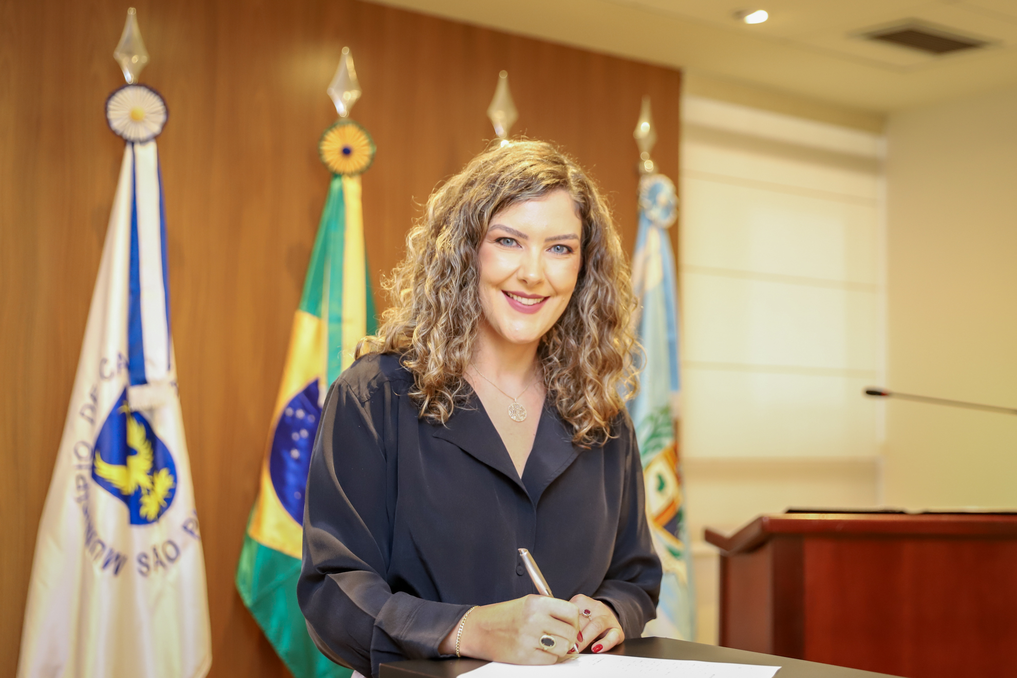 Juíza posa para foto, segurando a caneta em frente ao seu termo de posse.