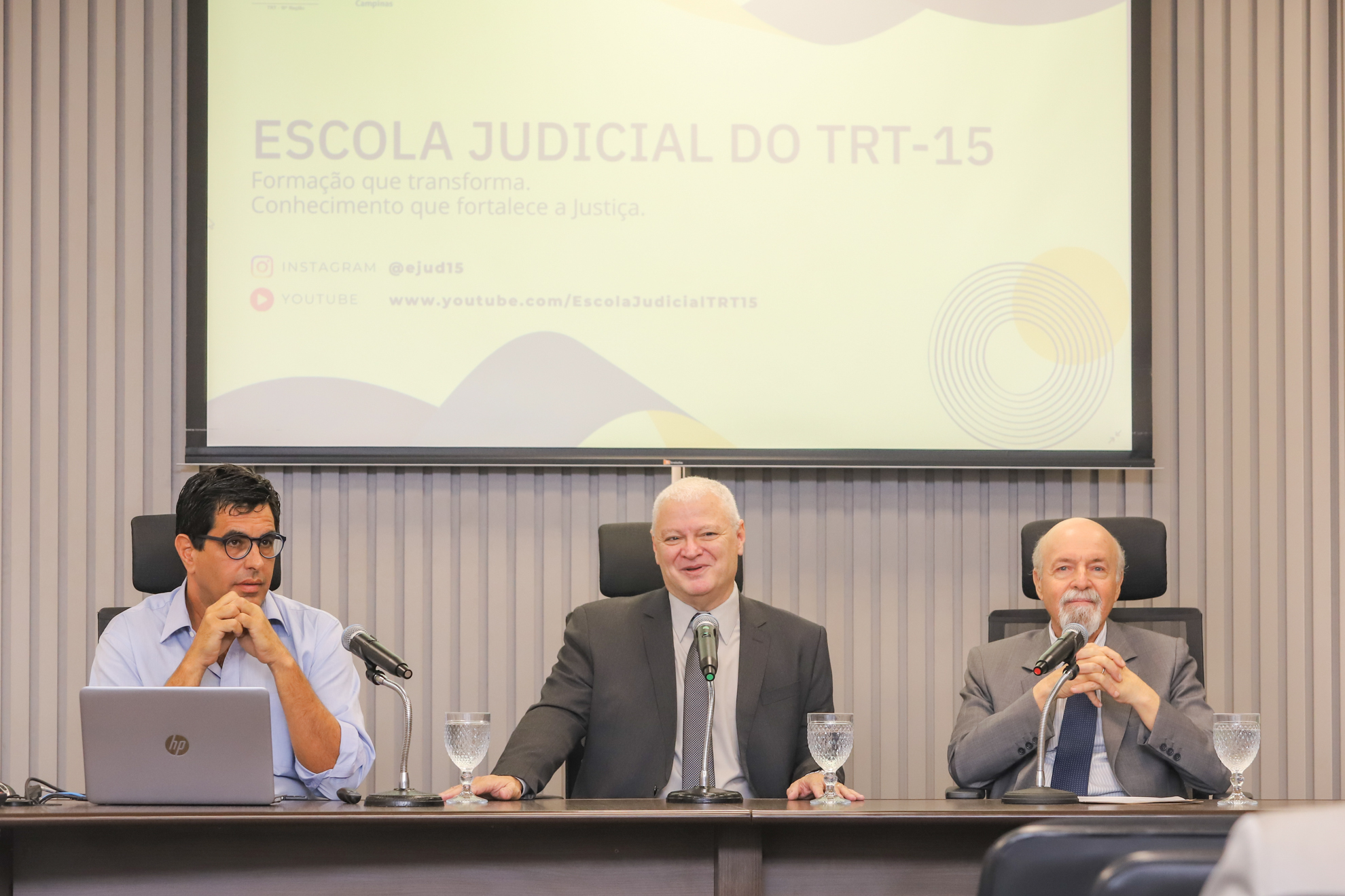 três homens sentados em uma mesa de frente para uma pequena platéria
