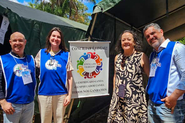 dois homens e duas mulheres posam em pé com um banner de um evento entre eles