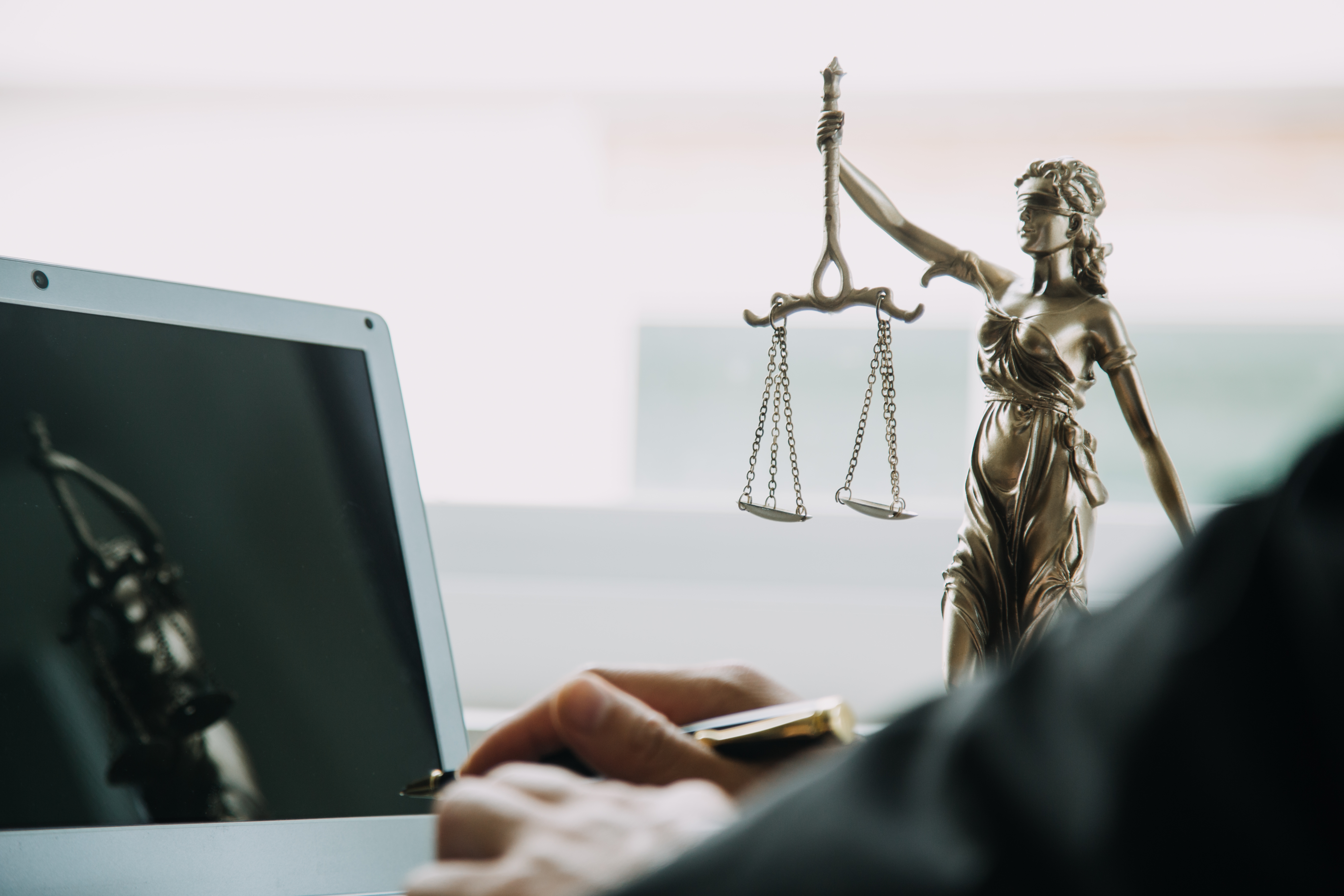 homem dedilha notebook com a imagem da justiça ao fundo