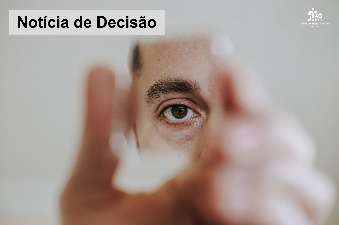 quadro cinza com homem que segura um pequeno espelho com as mãos desfocadas, que exibe um de seus olhos