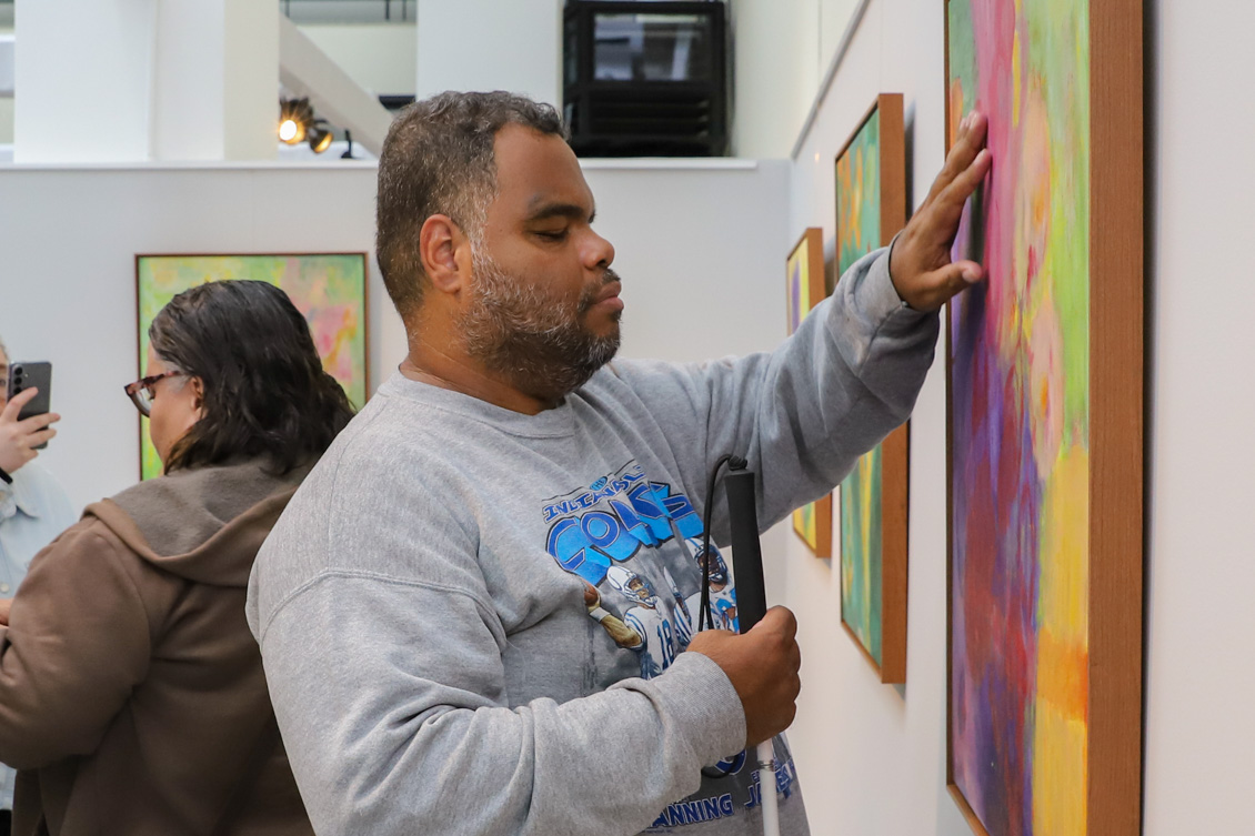 Um rapaz deficiente visual passa a mão em uma das obras da artista.