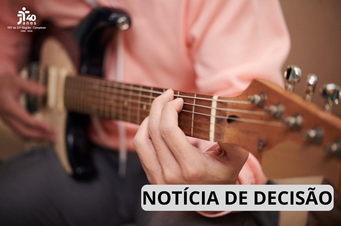 Um homem toca um violão, o foco está na sua mão. 