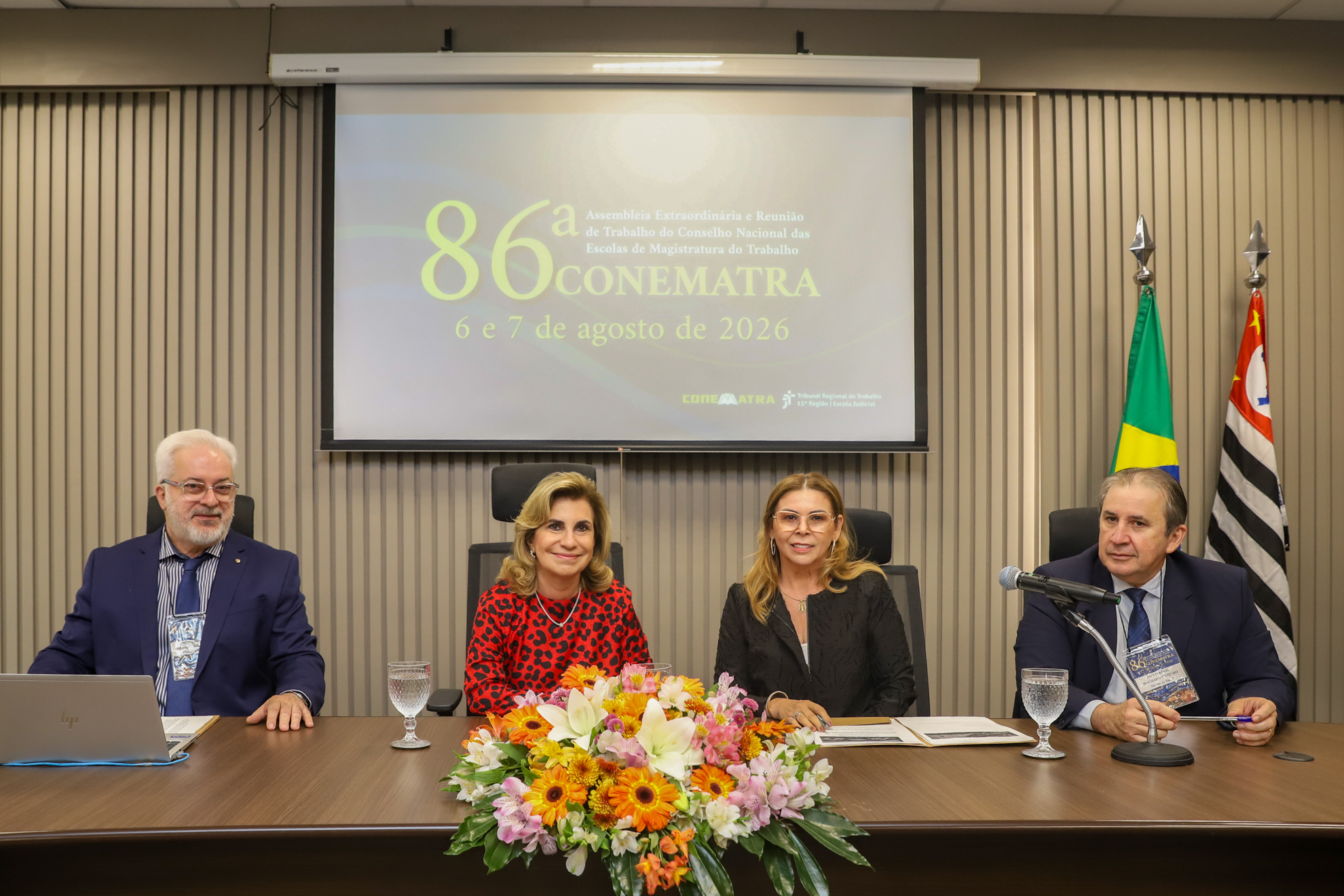 Quatro pessoas estão sentadas e posam para a foto, duas mulheres e dois homens.