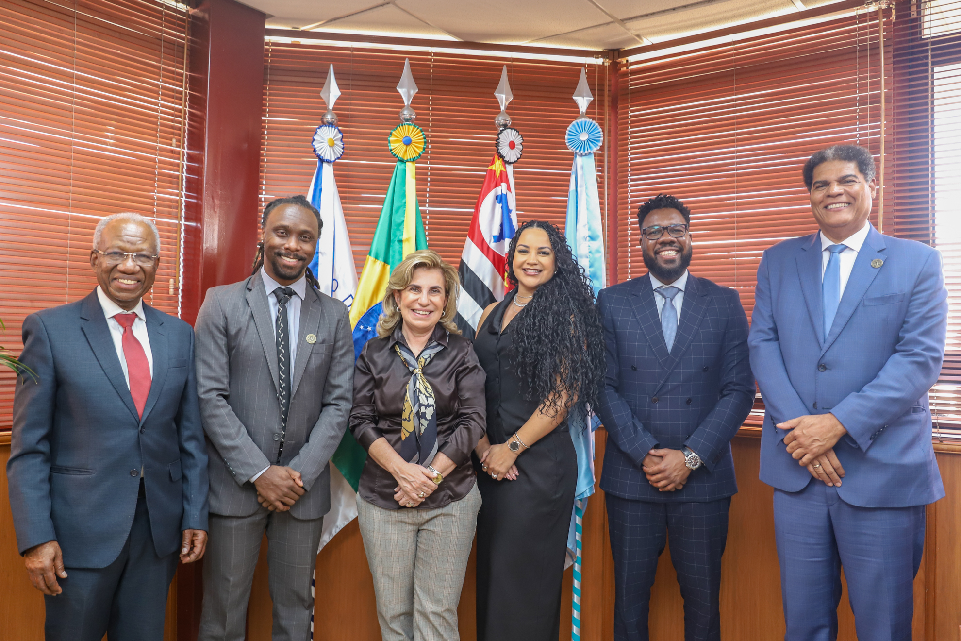 foto posada dos visitantes com a Dra. Ana Paula em frente as bandeiras em seu gabinete