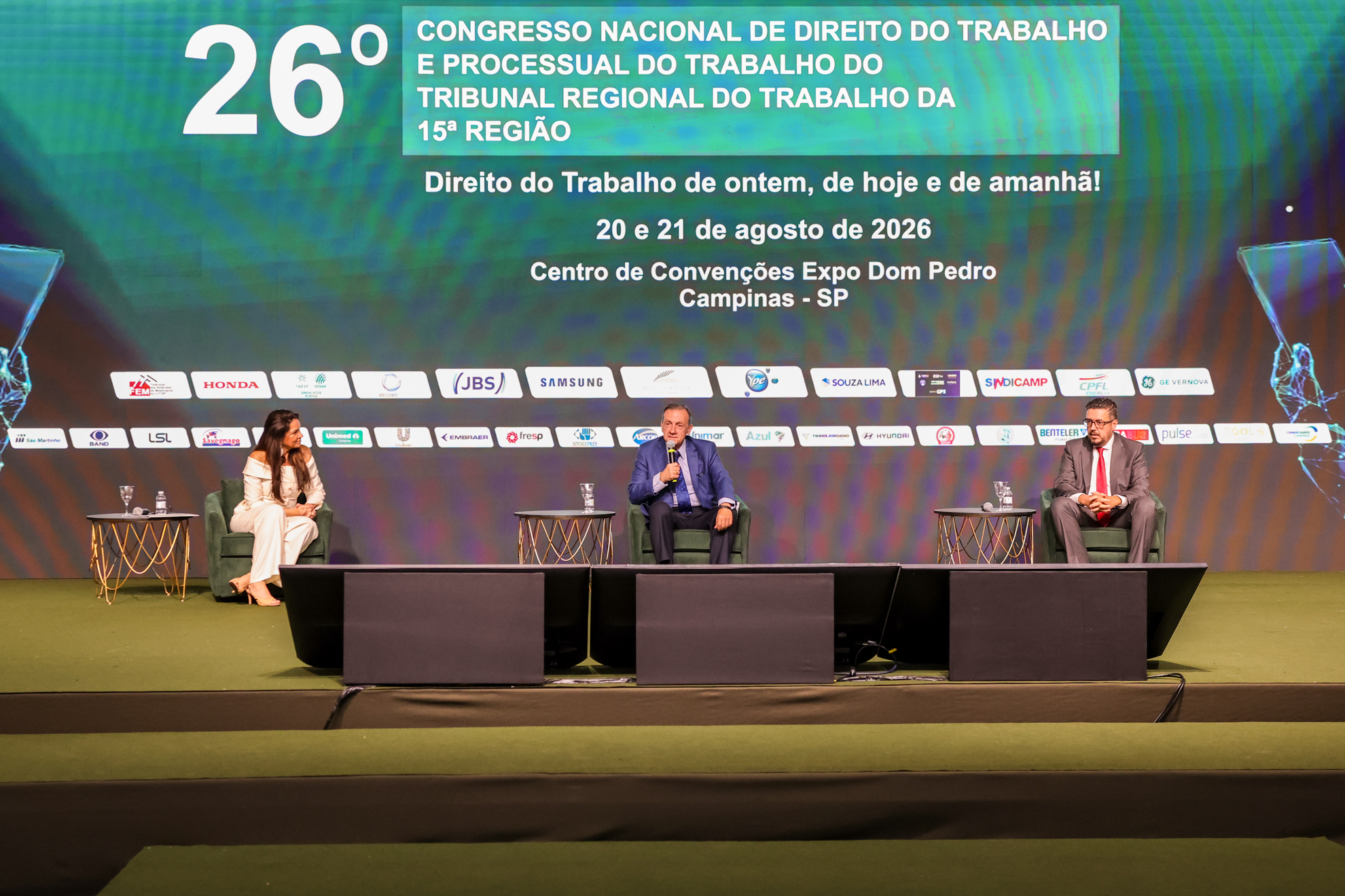palestrantes e mediador no palco sentados em poltronas, com telão sobre o congresso ao fundo
