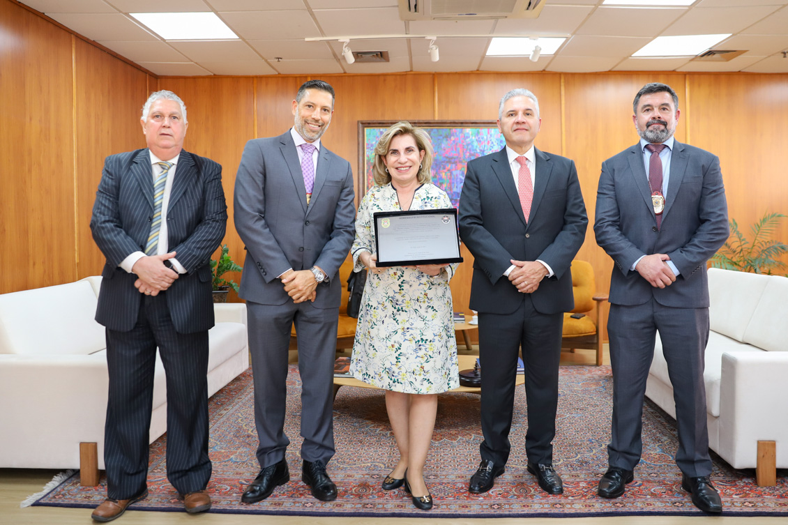foto posada dos participantes do encontro, todos de pé, e Dra. Ana Paula segurando a placa