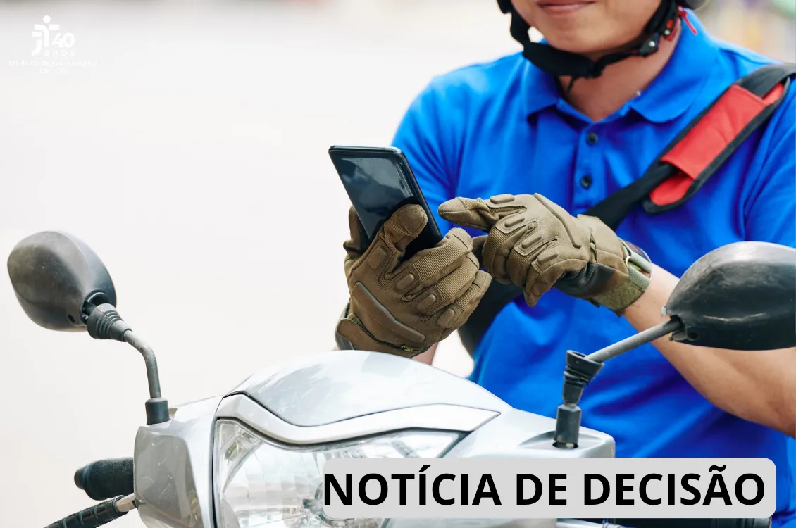 Um homem sentado na moto mexendo no celular.
