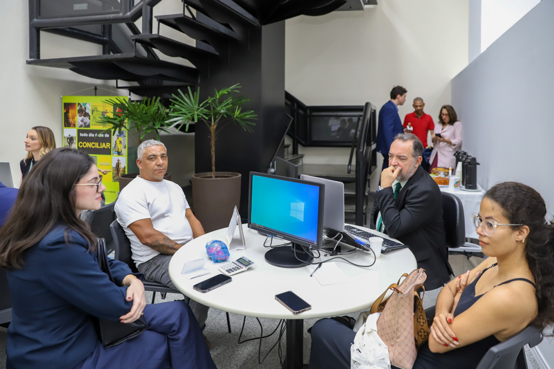 "Dois homens e duas mulheres em mesa redonda de conciliação, de frente para microcomputadores"