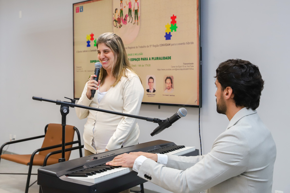 "Mariana canta ao microfone, sendo acompanhada pelo professor Daniel no teclado"