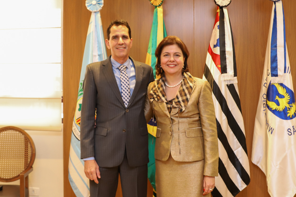 "Dra. Scynthia posa para foto em frente as bandeiras, com o marido, Dr. Alessandro"