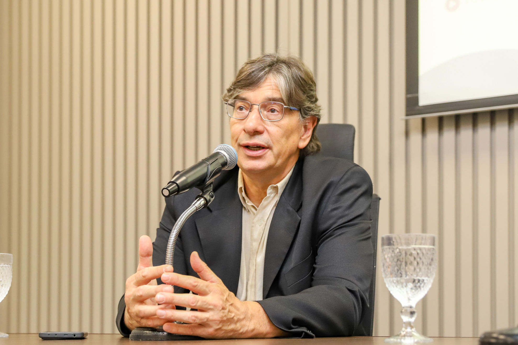 "Pochmann está sentado à mesa alta, falando ao microfone"