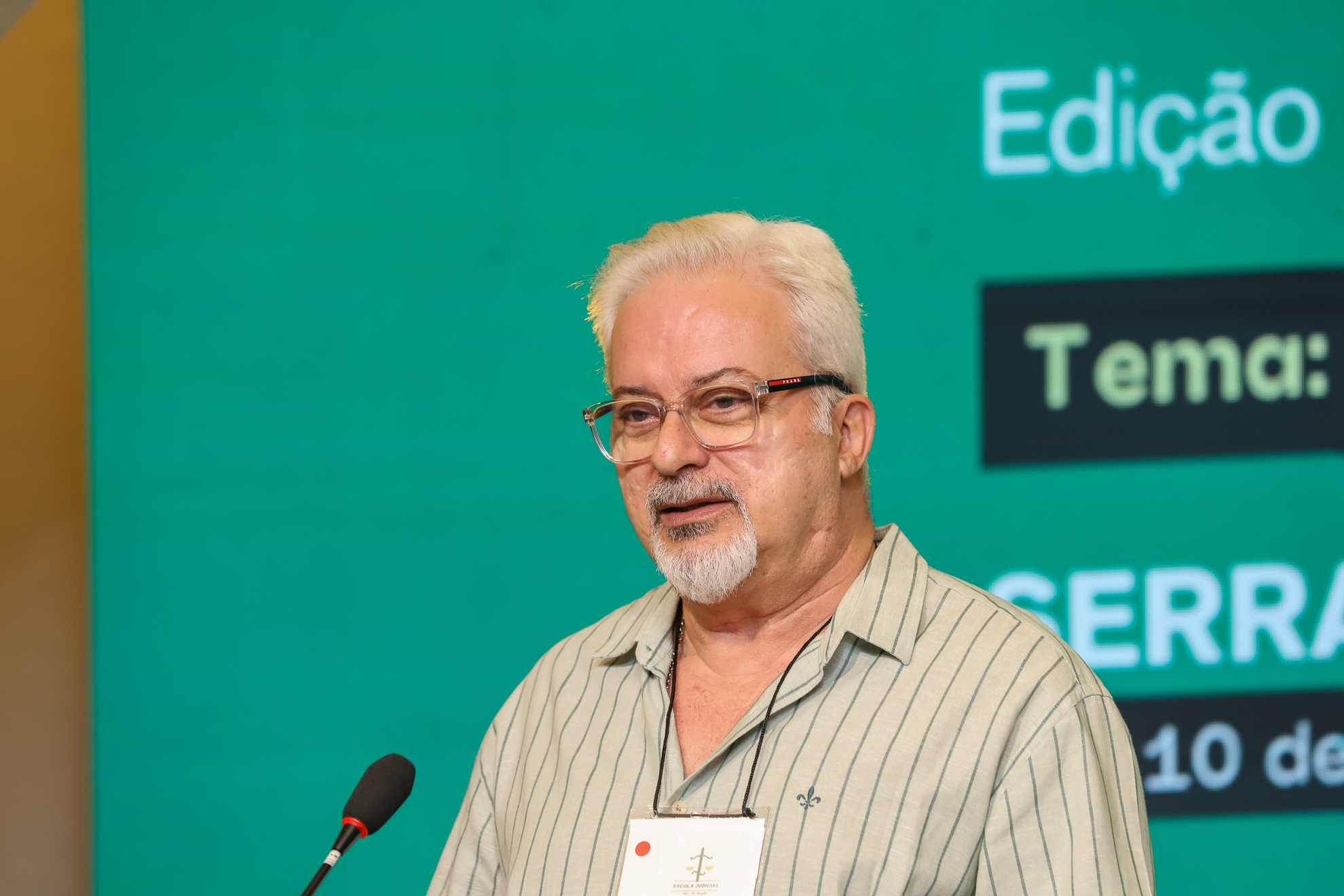 "Dr. Luiz Felipe Lobo fala ao microfone. Ao fundo painel verde"