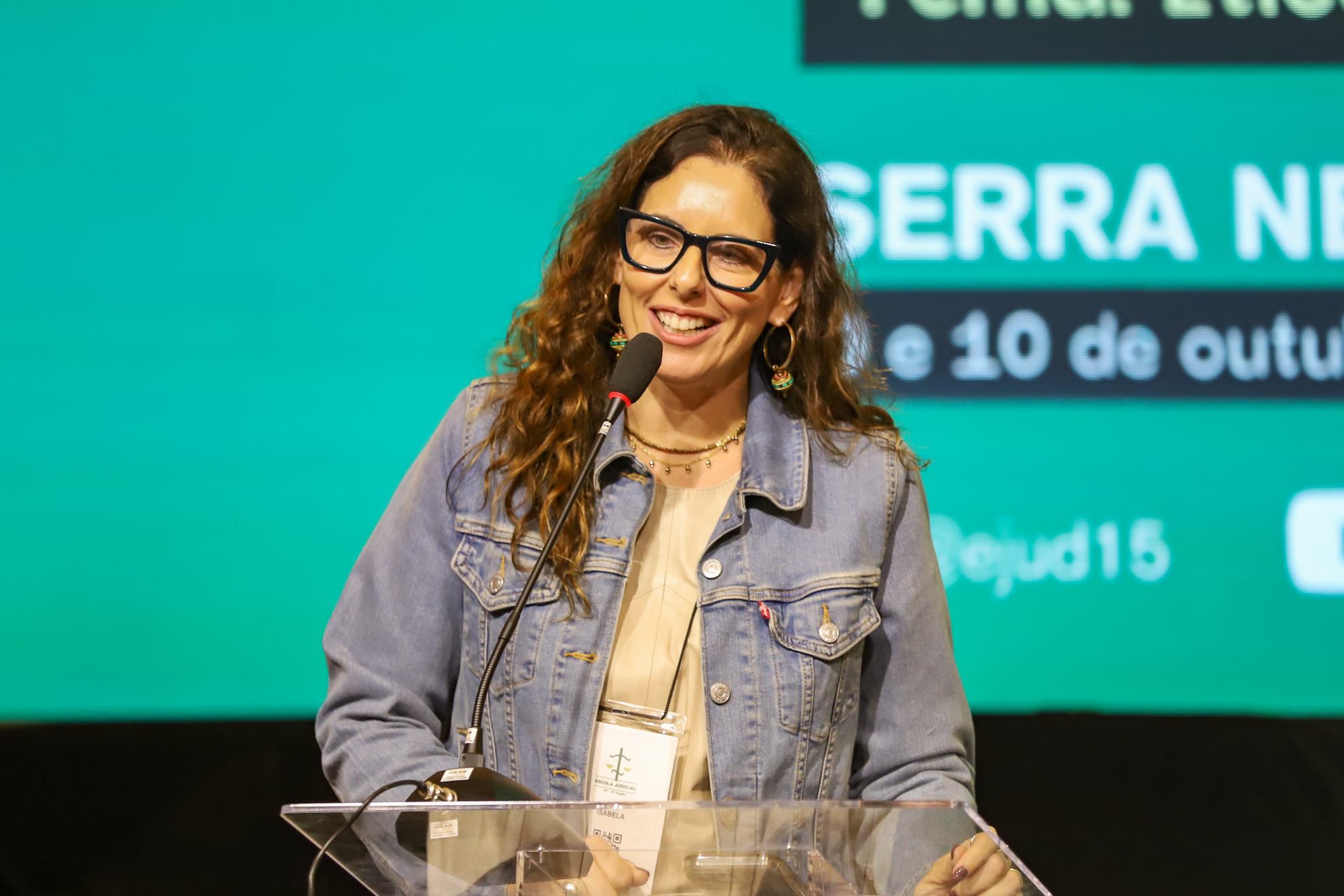 "Dra. Isabela fala ao microfone. Ao fundo painel verde"