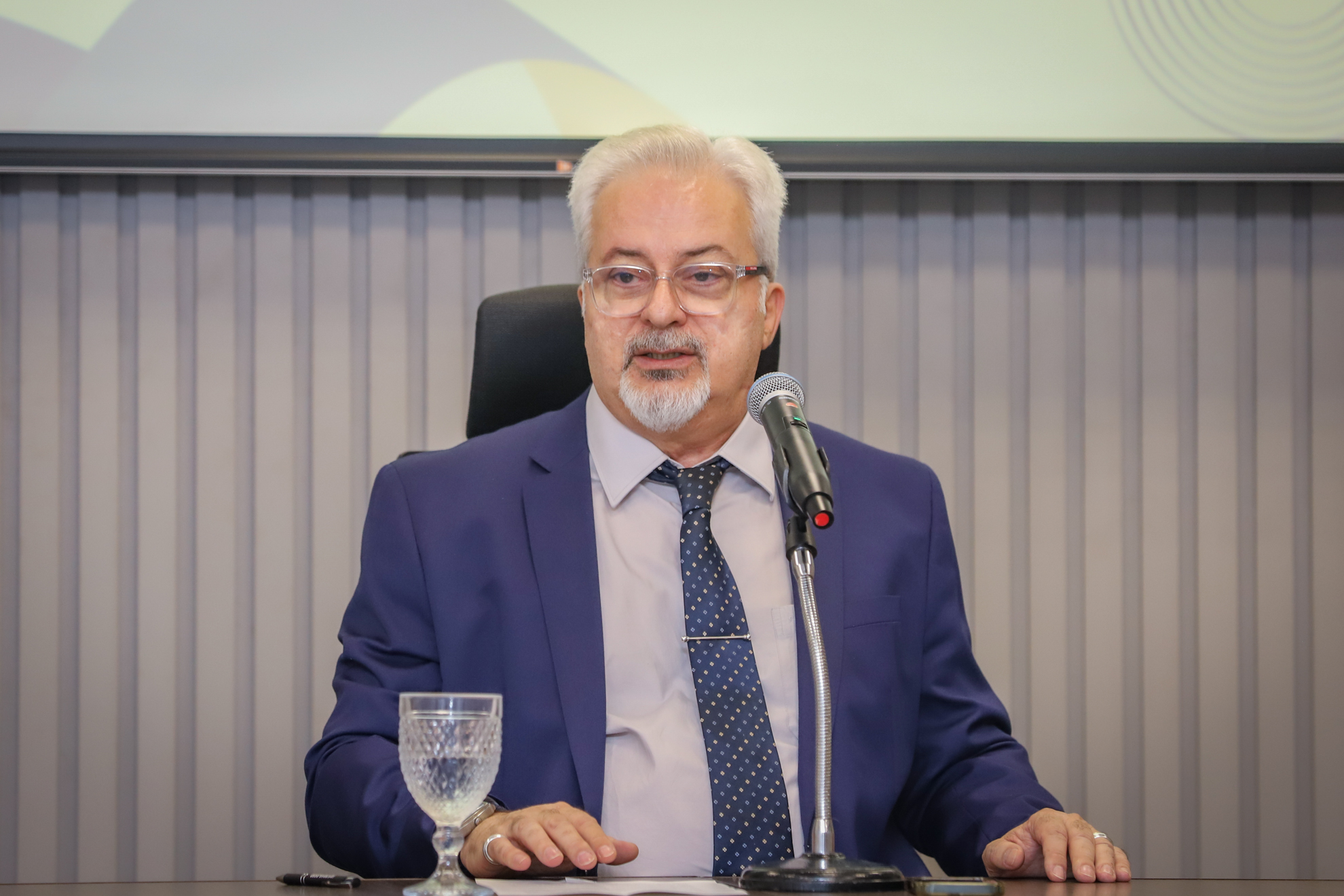"Dr. Lobo fala ao microfone, sentado à mesa de trabalhos"