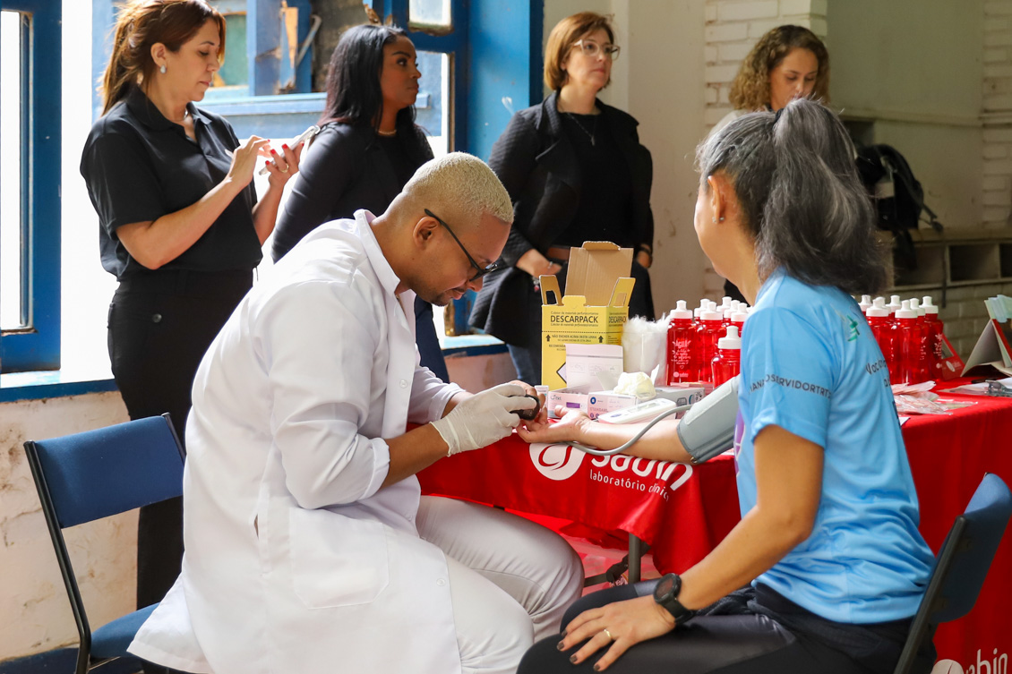 "Mesa de trabalhos do Sabin, com profissional fazendo medição de glicemia de servidora"