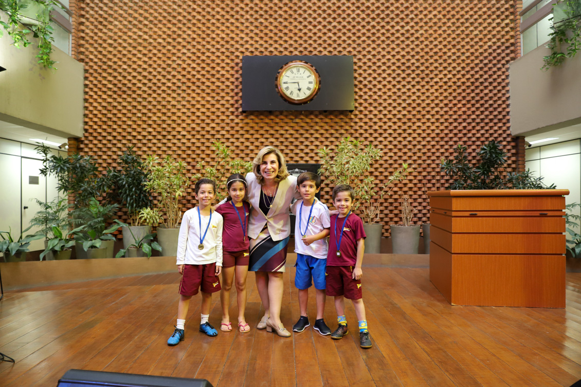 "Dra. Ana Paula posa para foto ao lado de quatro crianças que têm medalhas penduradas no pescoço"