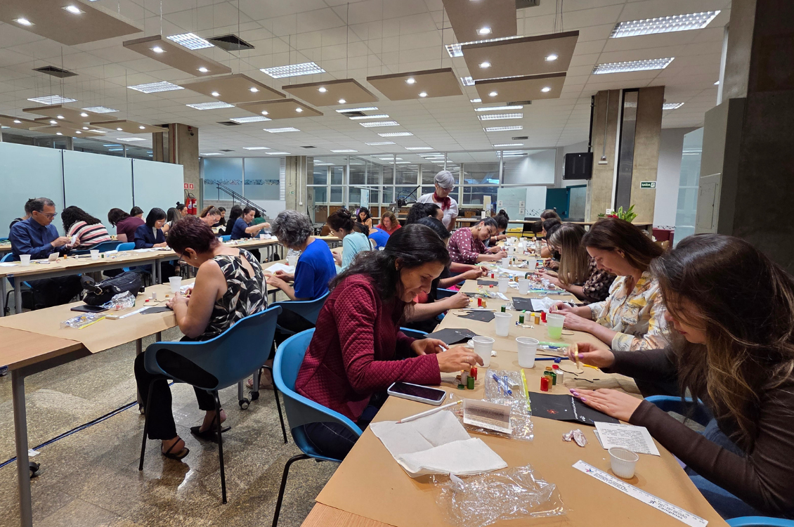 "No Colabora, dezenas de servidores participam de oficina de pontilhismo sentados à mesa de trabalhos"