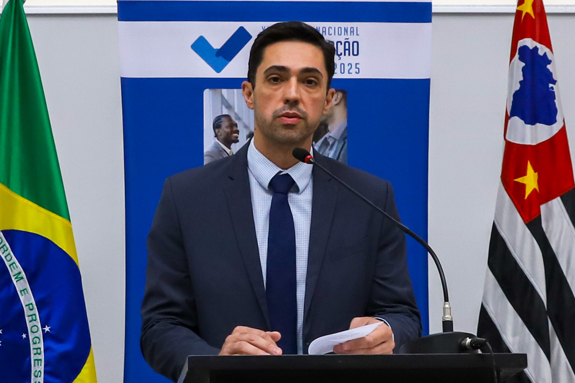 "Juiz Francisco fala ao microfone no púlpito de madeira. Ao fundo, banner alusivo à campanha, entre bandeiras do Brasil e do Estado de São Paulo"