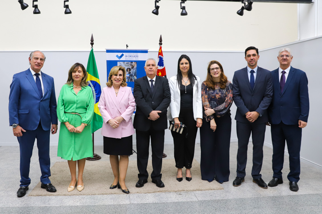 "Dr. Fabio, Dra. Alvamari, Dra. Ana Paula, Dr. Helcio, Dra. Ana Claudia, Dra. Luciana, Dr. Francisco e Dr. Edison estão de pé, posando para foto, em frente ao banner alusivo da campanha e as bandeiras do Brasil e de São Paulo"