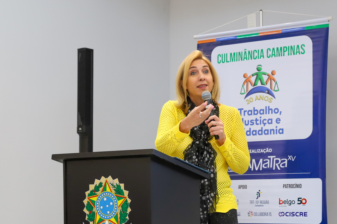 "Secretária Patrícia fala ao microfone, no púlpito, em frente a um banner azul sobre o projeto"