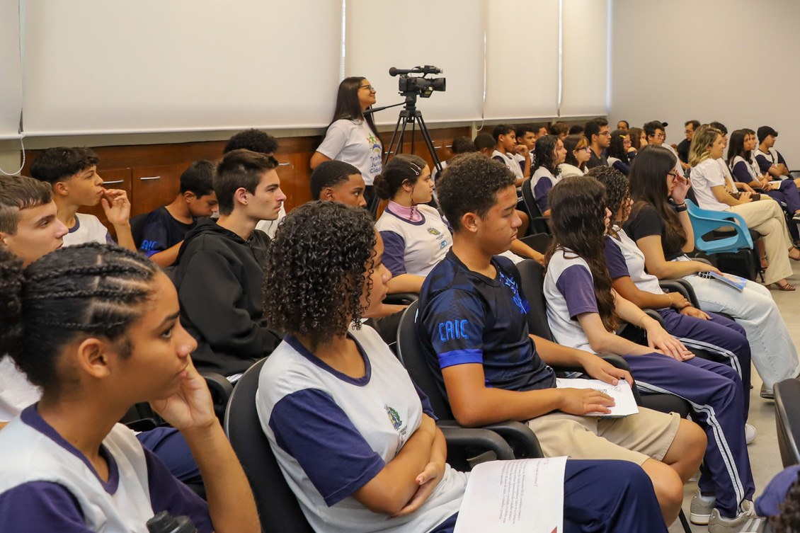 "Alunos estão sentados nas cadeiras azuis no auditório"