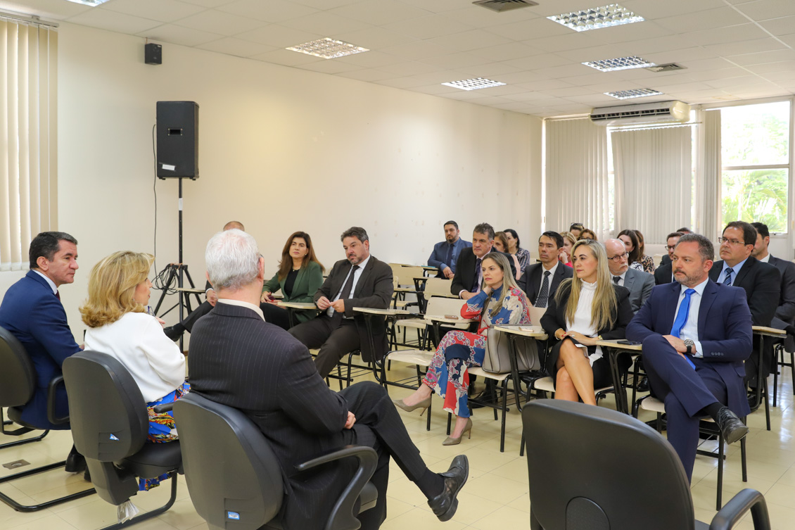 "Imagem geral do auditório com os magistrados sentados, observando os membros da alta administração, que estão à esquerda da tela, de costas"