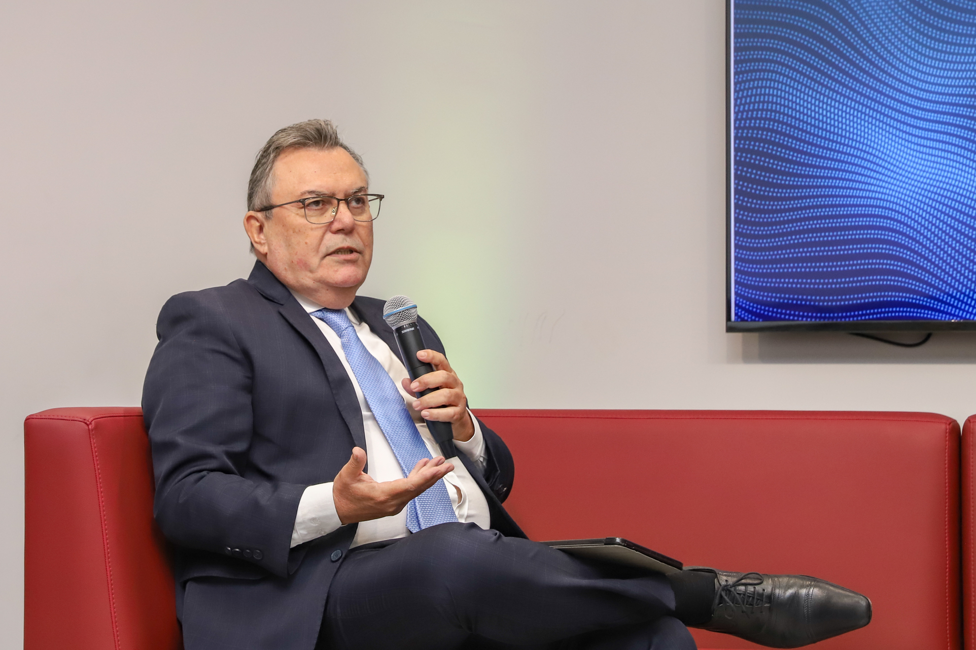 "Dr. Levi está sentado em um sofá vermelho, falando ao microfone"